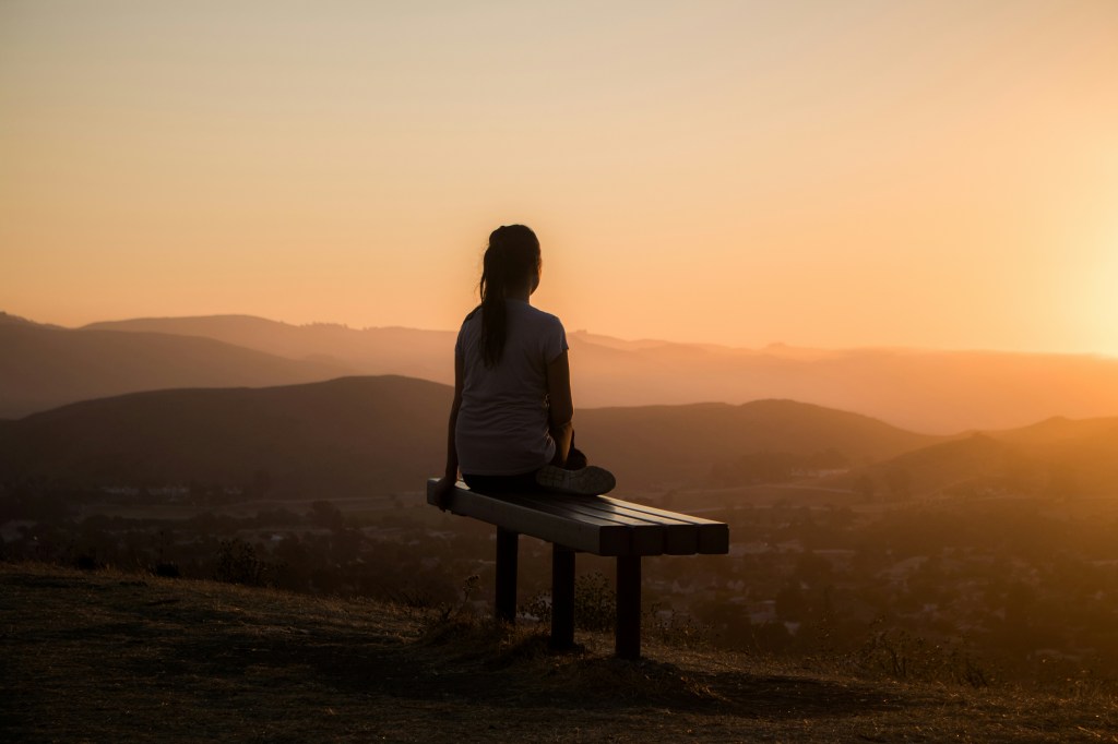 Person looking at rising sun from a hilltop. this represents hope. 